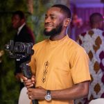 Male videographer in Nigerian attire captures joyous event with a camera.