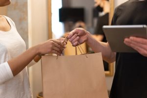 Close-up of hands exchanging a shopping bag indoors, symbolizing modern retail and technology.